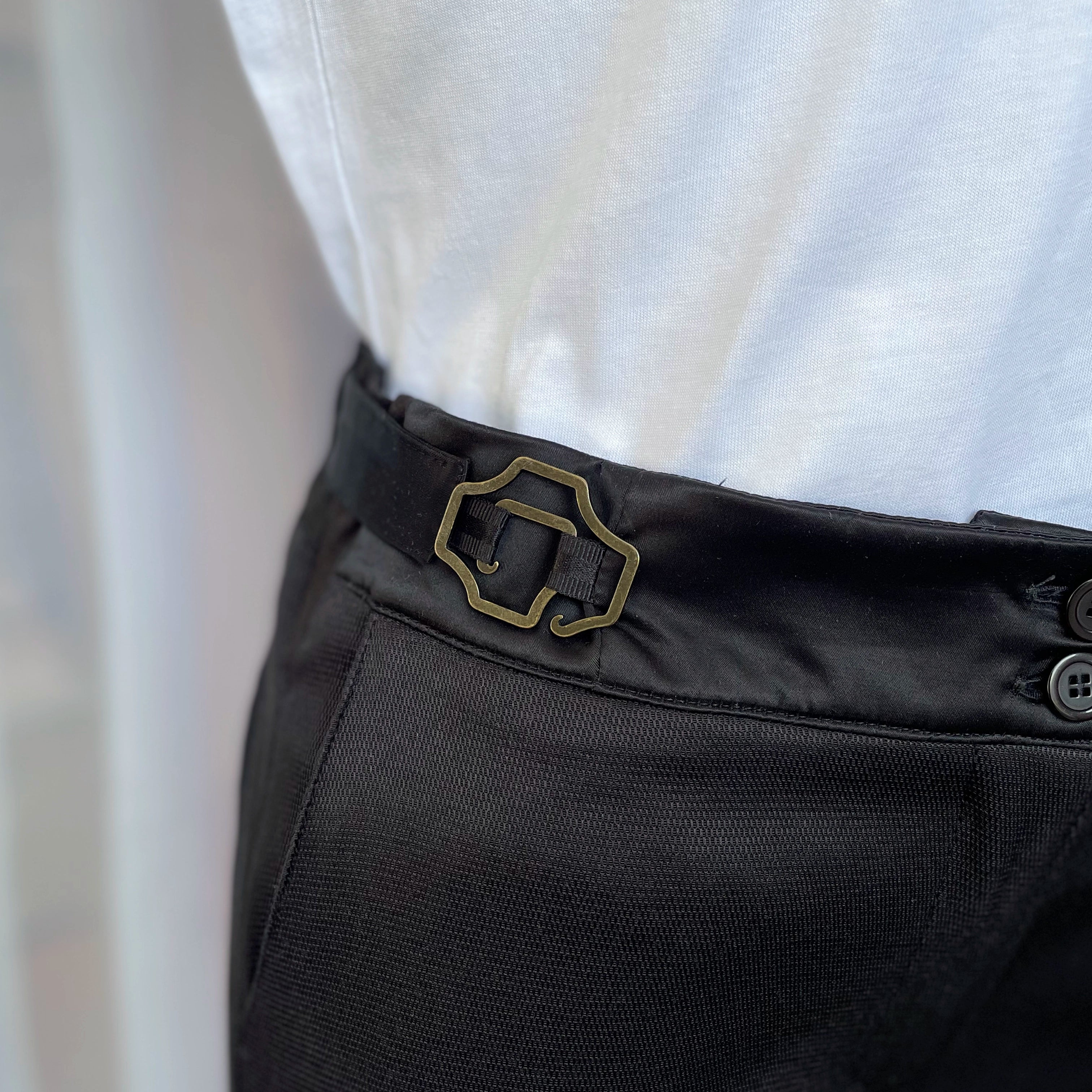 Zoom sur les boucles ajustables, La Justine, modèle baroque laiton vieilli permettant de resserrer la taille du pantalon, création Asur.