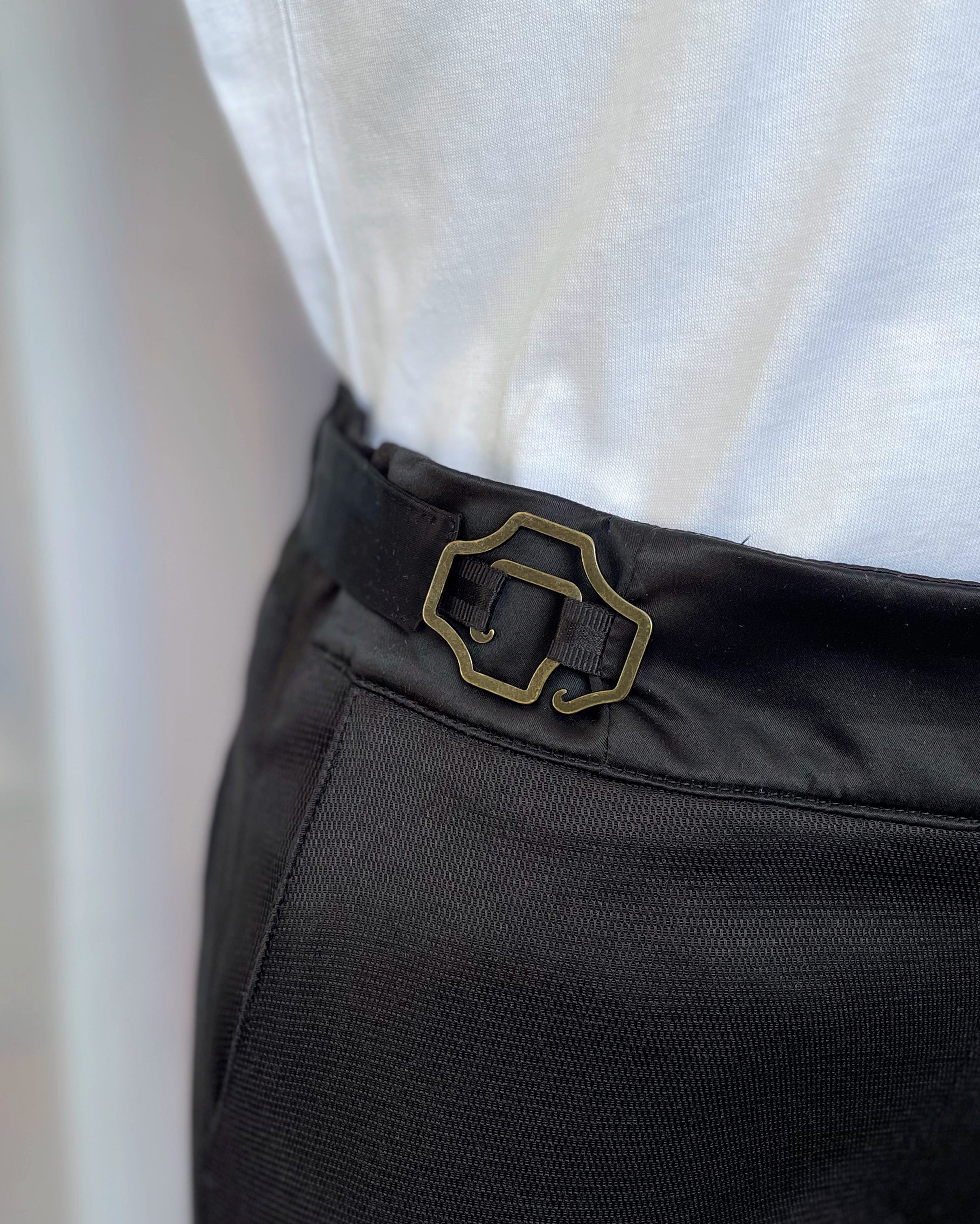 Zoom sur les boucles ajustables, La Justine, modèle baroque laiton vieilli permettant de resserrer la taille du pantalon, création Asur.
